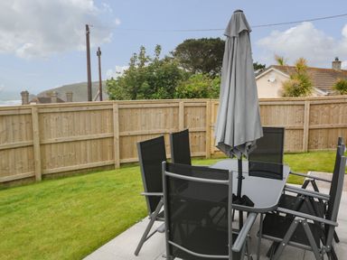 A patio with a table and six chairs and a closed umbrella in a fenced garden at 3 Praa Cove in Praa Sands