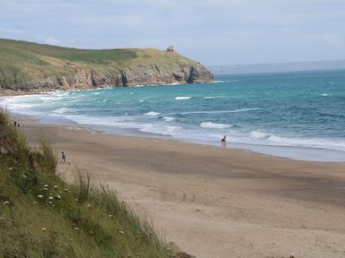 A sandy beach with people walking near the water and cliffs in the background at 3 Praa Cove in Praa Sands