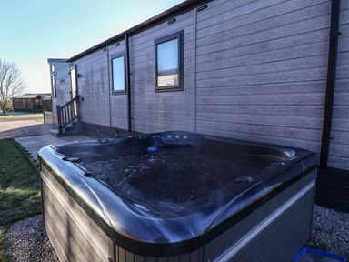 An outdoor hot tub next to a grey wooden cabin with windows at Owl's Nest in Newton on Derwent near Wilberfoss