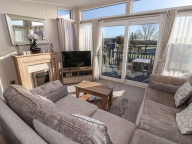 A living room with couches a coffee table a TV a fireplace and glass doors leading to a deck at Owl's Nest in Newton on Derwent near Wilberfoss