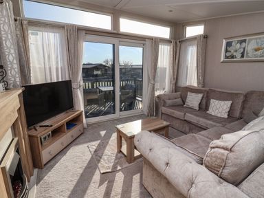 A living room with a sectional sofa a wooden coffee table a flat screen tv on a wooden stand sliding glass doors leading to an outdoor patio at Owls Nest in Newton on Derwent near Wilberfoss