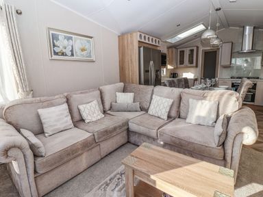 A living room with a corner sofa and a wooden coffee table next to an open kitchen with dining table at Owl's Nest in Newton on Derwent near Wilberfoss