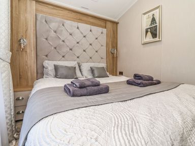 A bedroom with a bed linens pillows folded towels a tufted headboard bedside lights and framed art at Owls Nest in Newton on Derwent near Wilberfoss
