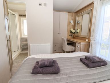 A bedroom with a bed covered in folded towels a dressing table with a mirror and chair and a bathroom in the background at Owls Nest in Newton on Derwent near Wilberfoss