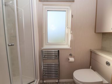 A bathroom with a shower cabin, window, heated towel rail, toilet, and countertop at Owl's Nest in Newton on Derwent near Wilberfoss