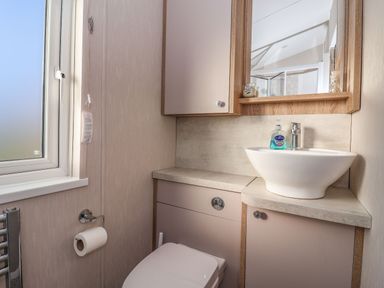 A bathroom with a toilet, a sink with a faucet, a mirror above the sink, a window, and a toilet paper holder at Owl's Nest in Newton on Derwent near Wilberfoss