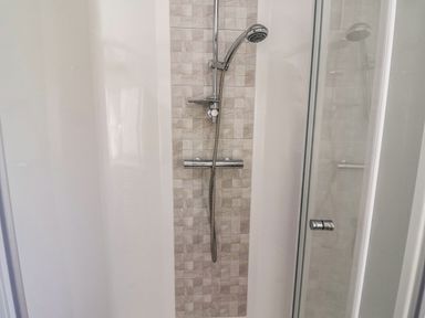 A shower area with a handheld showerhead and tiled wall at Owls Nest in Newton on Derwent near Wilberfoss