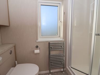 A bathroom with a toilet paper holder and a heated towel rail near a window and a shower enclosure at Owl's Nest in Newton on Derwent near Wilberfoss