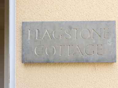 A metal sign with the text flagstone cottage on a textured beige wall at Flagstone Cottage Upper Swell near Stow-On-The-Wold