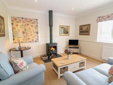 A living room with a wood burning stove a television on a stand two sofas and a coffee table at Flagstone Cottage in Upper Swell near Stow-On-The-Wold