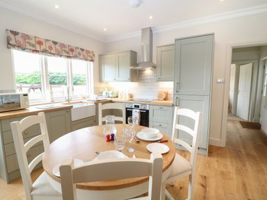 A kitchen with a round dining table set for a meal and cabinetry at Flagstone Cottage in Upper Swell near Stow-On-The-Wold