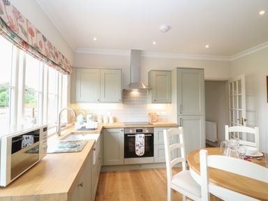 A kitchen with wooden countertops green cabinets and a dining table with white chairs at Flagstone Cottage in Upper Swell near Stow-On-The-Wold