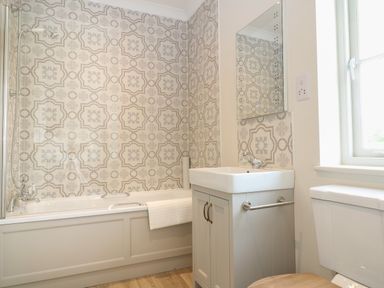 A bathroom with a bathtub shower combination sink with cabinet and mirror and a toilet near a window at Flagstone Cottage in Upper Swell near Stow-On-The-Wold