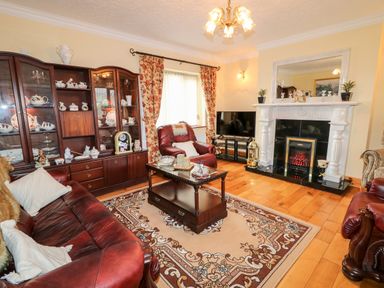 A living room with brown leather sofas a wooden cabinet with china a fireplace a television and floral curtains at Derriens Farmhouse Letterbreen County Fermanagh
