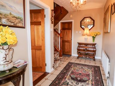 An entryway with a patterned rug on tiled floor wooden doors a staircase an ornate wooden chest with a lamp and flowers at Derriens Farmhouse Letterbreen County Fermanagh