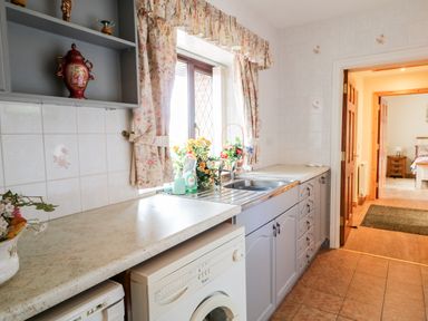 A kitchen with a washing machine a sink floral curtains and flowers at Derriens Farmhouse in Letterbreen County Fermanagh