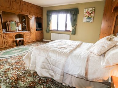 A bedroom with a bed near window and wooden wardrobes with dressing table at Derriens Farmhouse Letterbreen County Fermanagh