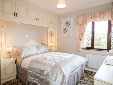A bedroom with a bed, bedside tables with lamps, a window with curtains, and a dresser at Derriens Farmhouse in Letterbreen County Fermanagh