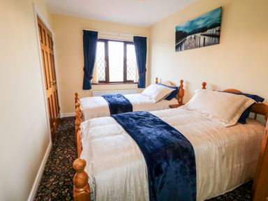 A bedroom with two single beds with blue runners and a window with blue curtains at Derriens Farmhouse in Letterbreen County Fermanagh