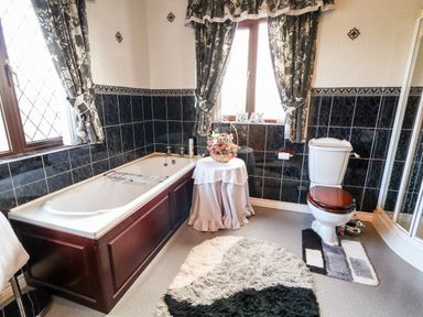 A bathroom with a bathtub wooden toilet seat table with flowers and patterned curtains at Derriens Farmhouse Letterbreen County Fermanagh