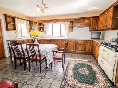 A kitchen with wooden cabinets a dining table with six chairs yellow flowers on the table and a patterned rug on the floor at Derriens Farmhouse Letterbreen County Fermanagh