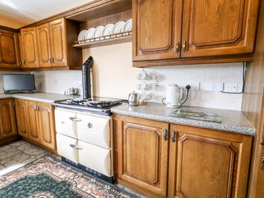 A kitchen with wooden cabinets a stove kettle cups and plates displayed at Derriens Farmhouse Letterbreen County Fermanagh