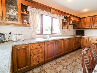 A kitchen with wooden cabinets a countertop a sink a toaster and floral curtains at Derriens Farmhouse Letterbreen County Fermanagh