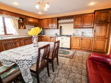 A kitchen with wooden cabinets a dining table with chairs and a vase of flowers at Derriens Farmhouse in Letterbreen County Fermanagh
