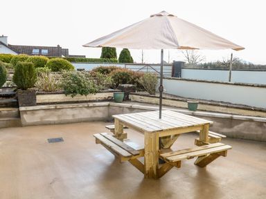 A wooden picnic table with an umbrella on a concrete patio with bushes and a low wall at Derriens Farmhouse in Letterbreen County Fermanagh