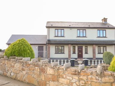 A two-story house with a stone wall and bushes in front at Derriens Farmhouse in Letterbreen County Fermanagh