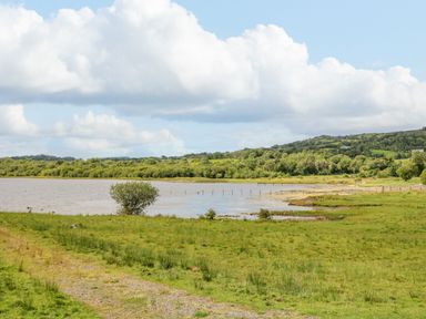 A grassy field next to a body of water with trees and hills in the background at Derriens Farmhouse in Letterbreen County Fermanagh