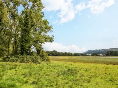 A grassy field with trees on the left and a body of water in the background under a partly cloudy sky at Derriens Farmhouse in Letterbreen County Fermanagh