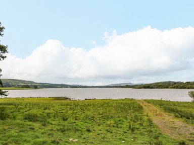 A grassy field leading to a lake with hills and trees in the background at Derriens Farmhouse Letterbreen County Fermanagh
