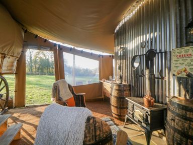 An interior view of a tent with chairs, a stove, wooden barrels, and a window overlooking grass at The Wagon at Burrow Hill in Ottery St Mary
