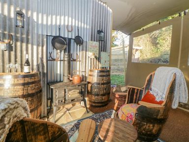 A seating area with wooden barrel chairs, a wood stove, and two barrels used as tables at The Wagon at Burrow Hill in Ottery St Mary