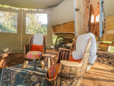 Two wooden chairs with cushions and throws inside a tent next to a wooden wagon at The Wagon at Burrow Hill in Ottery St Mary
