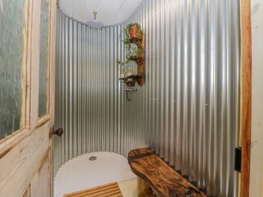 A shower area with corrugated metal walls a wooden bench a small wooden shelf with plants and soap at The Wagon at Burrow Hill in Ottery St Mary