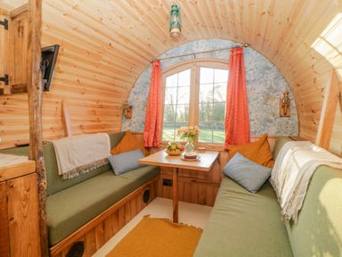A wooden interior with a small dining table between two green cushioned benches with pillows and throws at The Wagon at Burrow Hill in Ottery St Mary