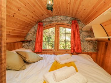 A small wooden bedroom with a bed pillows towels and a window with red curtains at The Wagon at Burrow Hill in Ottery St Mary