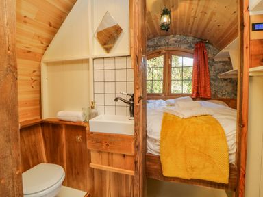 A small wooden room with a toilet sink and bed with yellow blanket and towels at The Wagon at Burrow Hill in Ottery St Mary