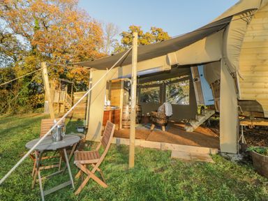 An outdoor seating area with a round wooden table and two chairs next to a covered wooden structure with stairs and a seating area at The Wagon at Burrow Hill in Ottery St Mary