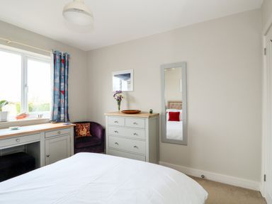A bedroom with a bed white bedspread a gray dresser a wall mirror and blue patterned curtains at The Lobster Pot in Overstrand