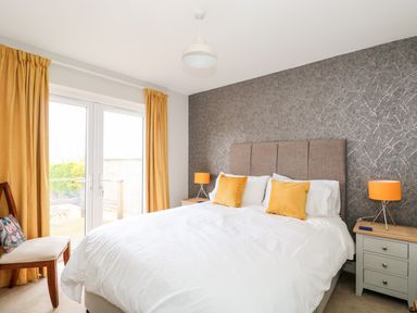 A bedroom with a bed white bedding yellow pillows bedside tables with lamps and yellow curtains at The Lobster Pot in Overstrand