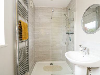 A bathroom with a walk-in shower a round mirror a white sink and a towel rail with a yellow towel at The Lobster Pot in Overstrand