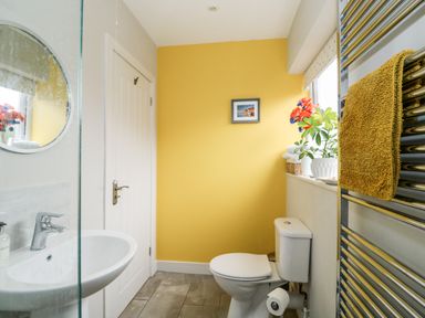 A bathroom with a white toilet and sink a yellow wall a towel on a heated rail and flowers on a windowsill at The Lobster Pot in Overstrand