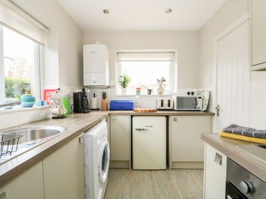 A kitchen with a washing machine a small fridge toaster microwave and coffee maker at The Lobster Pot in Overstrand
