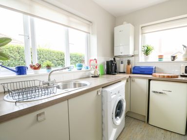 A kitchen with a sink a washing machine a small refrigerator and plants on the window sill at The Lobster Pot in Overstrand