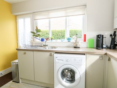 A kitchen with a washing machine under the counter a stainless steel sink and faucet a coffee machine and kitchen utensils on the countertop at The Lobster Pot in Overstrand