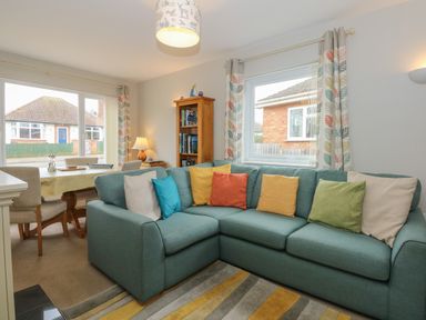 A living room with a blue corner sofa and colorful cushions near a dining table with chairs at The Lobster Pot in Overstrand