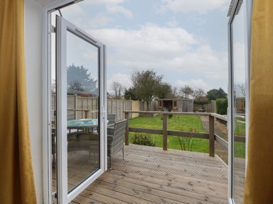 A wooden deck with outdoor furniture overlooking a fenced garden with a shed at The Lobster Pot in Overstrand